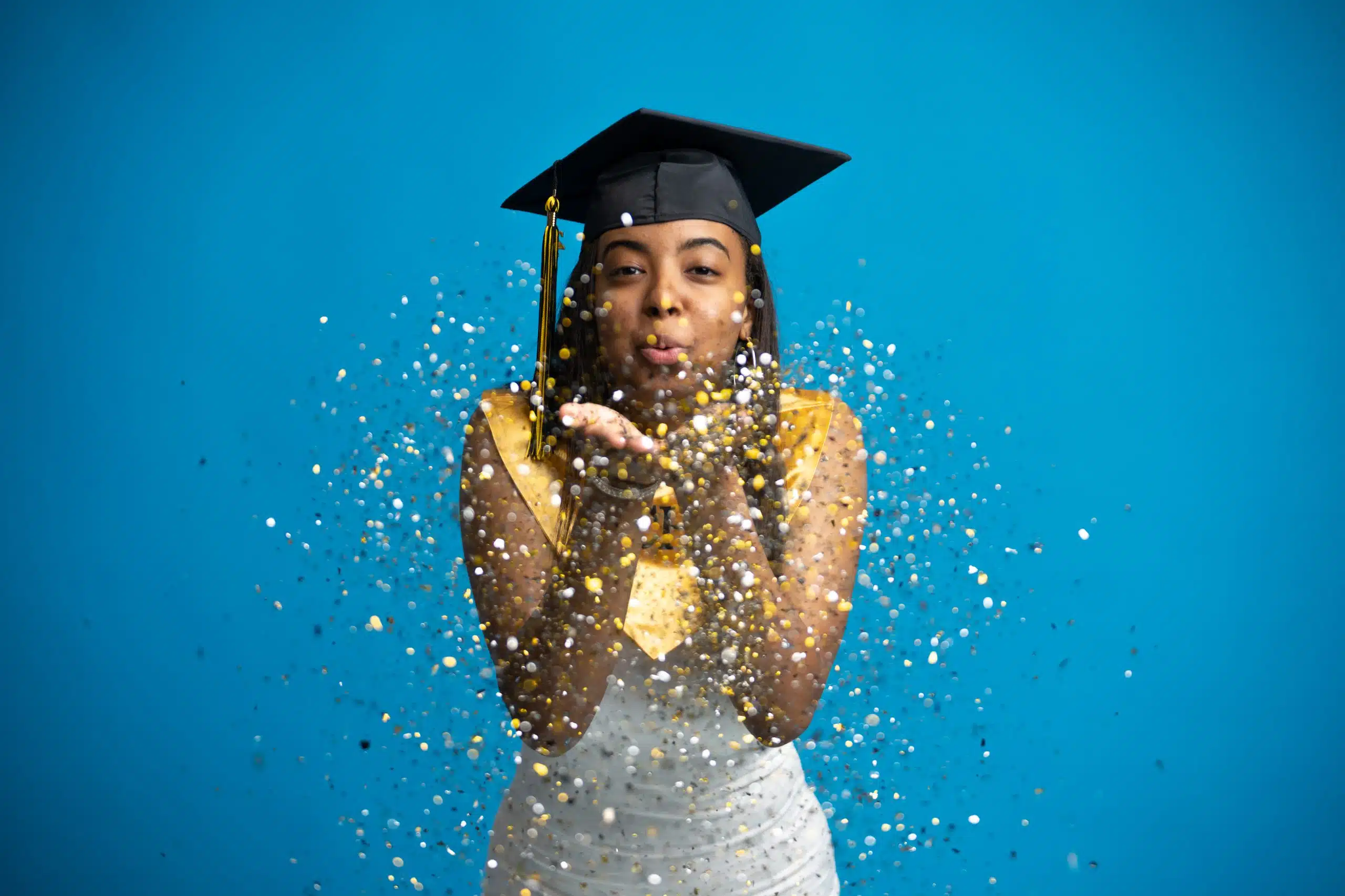 Girl blowing confetti for her graduation photos, she is located in a photography studio in Greenville, NC.