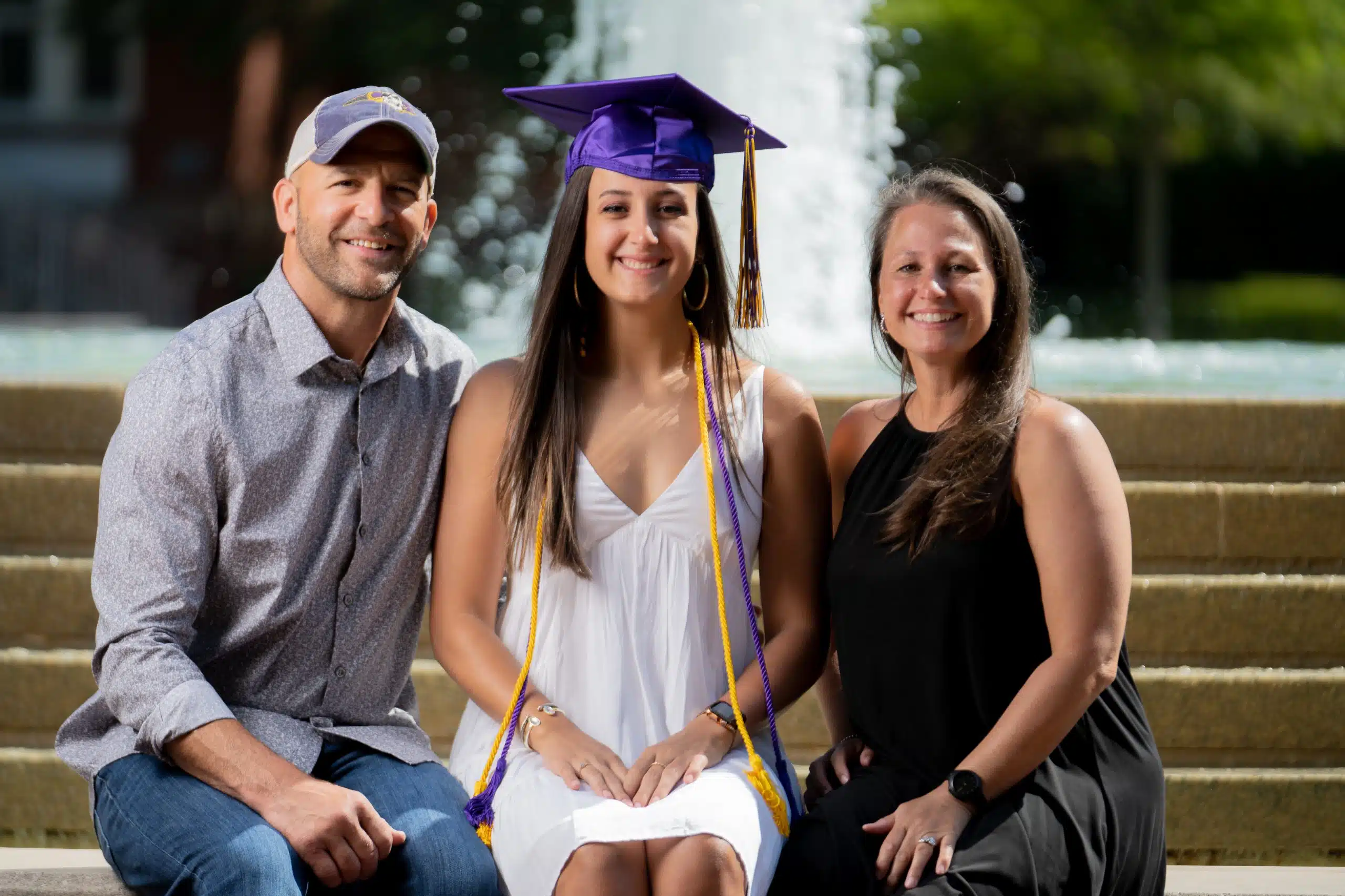 Girl posing with her mom and dad in front of the East Carolina University College fountain located on ECU campus. While taking her Graduation photos.