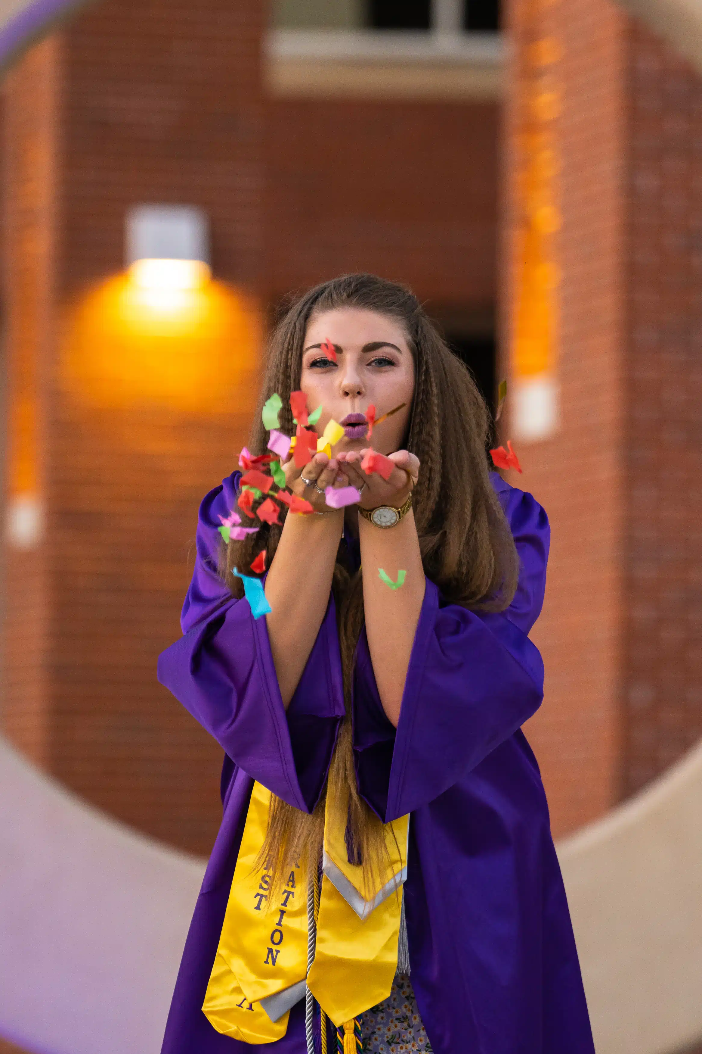 Girl blowing confetti for her Graduation photos, while being on ECU Campus. She is standing in front of East Carolina University College new ECU sign