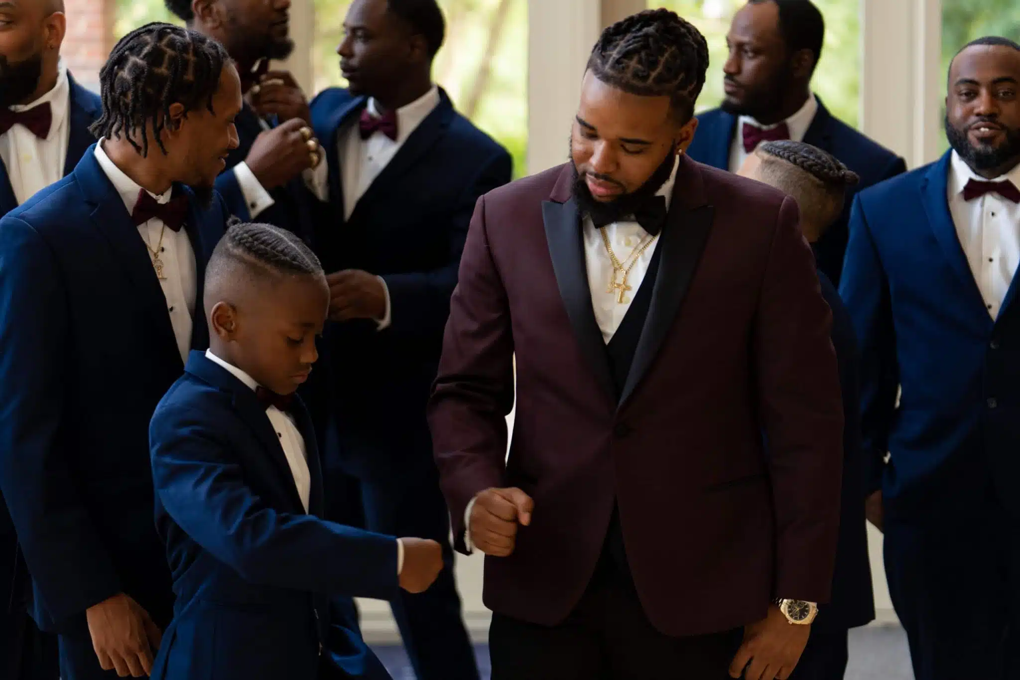 Man and son give each other a pound at the father's wedding in charlotte, nc wedding venue. The man is wearing a red suit with a black tie for his wedding day. Planning your first wedding starts here.