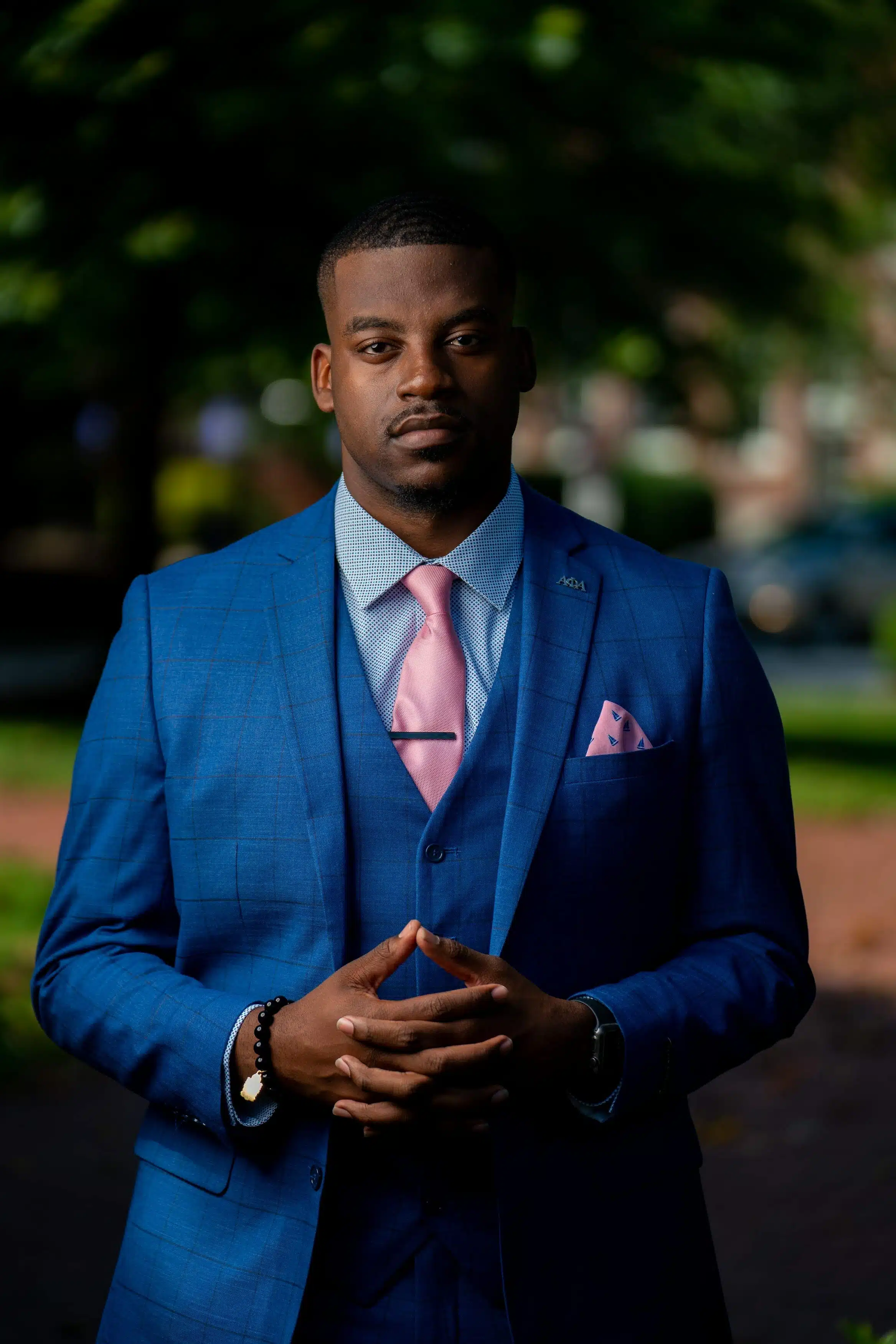 Black man wearing a blue suit with a pink tie. Posing outside of ECU Campus for his Graduation Photos.